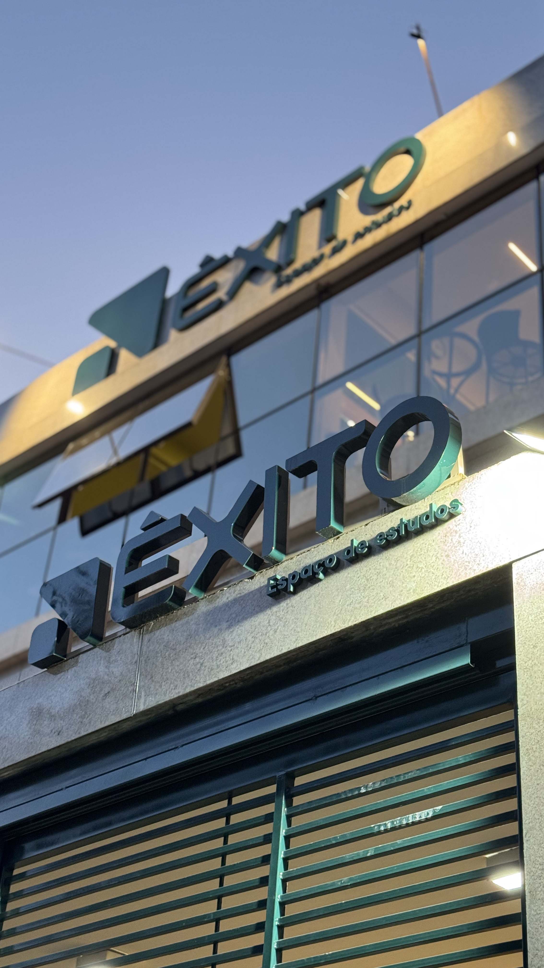 Letreiro Êxito Espaço de Estudos na fachada iluminado ao entardecer