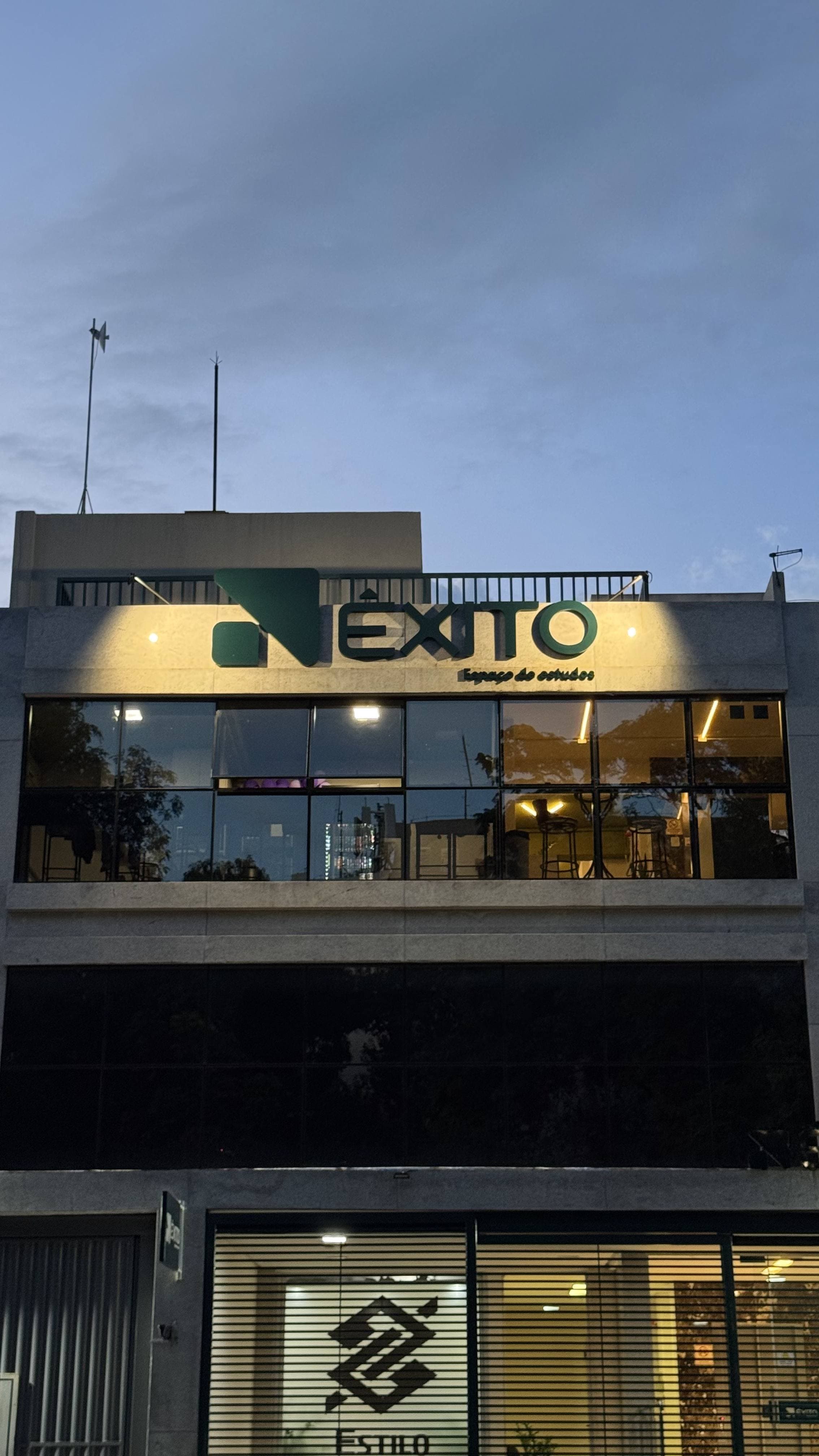 Fachada da Êxito iluminada ao entardecer com interior visível pelas janelas