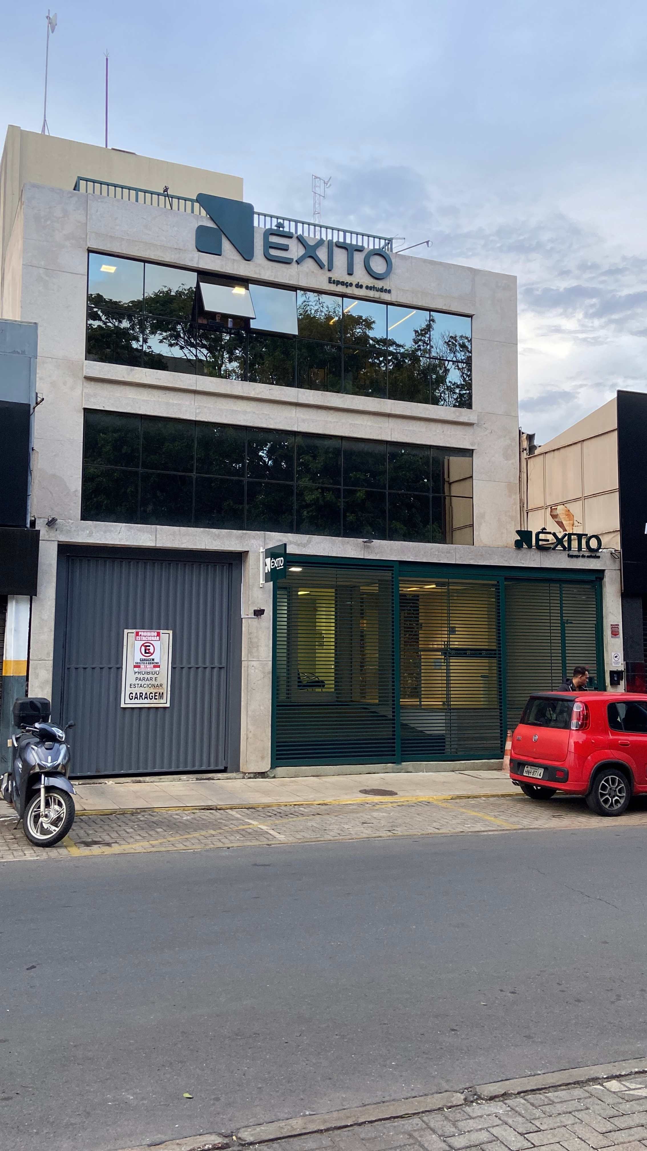 Fachada frontal da Êxito ao entardecer com moto e carro vermelho