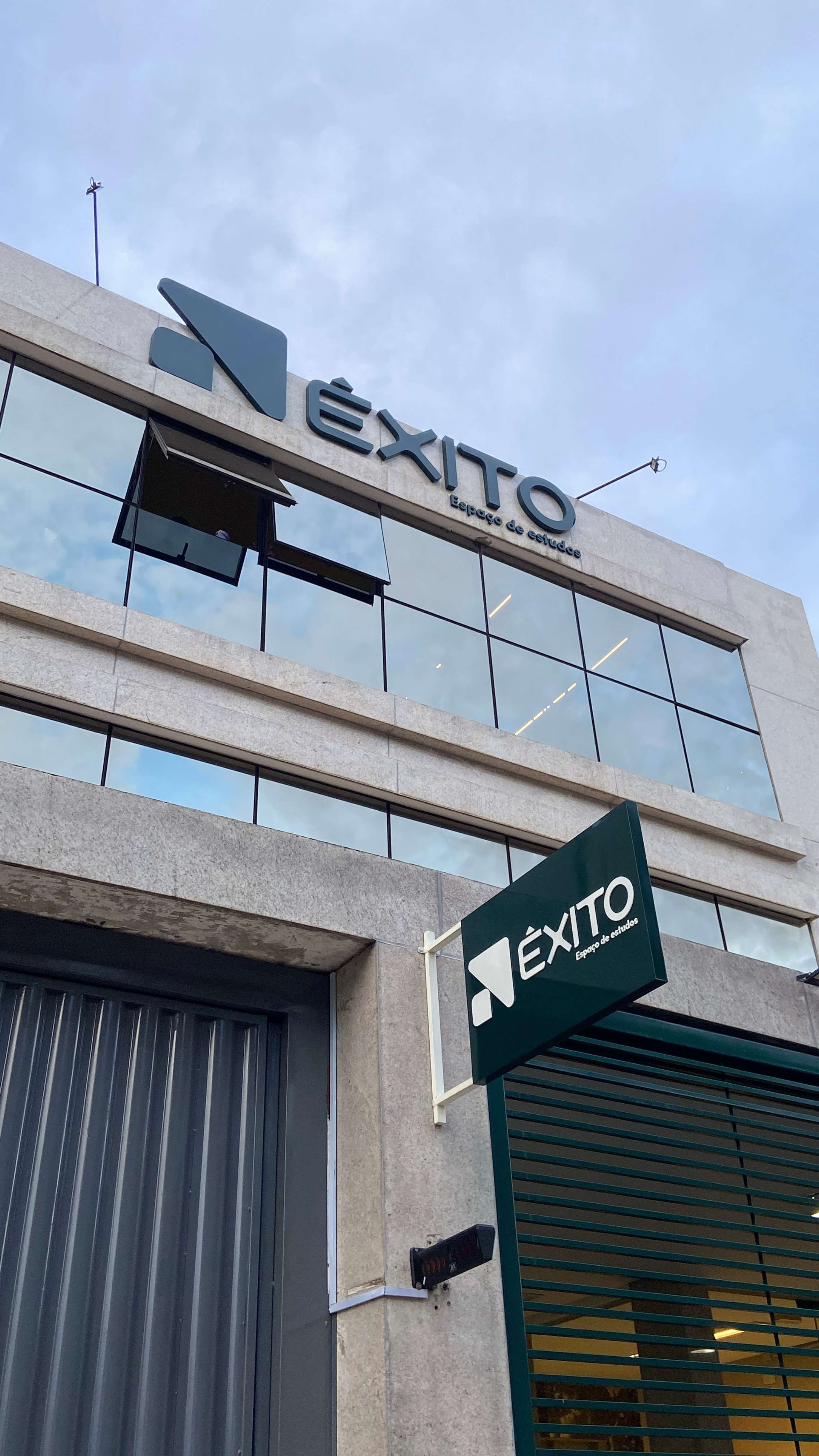 Fachada frontal de dia com letreiro e placa suspensa, ângulo ascendente