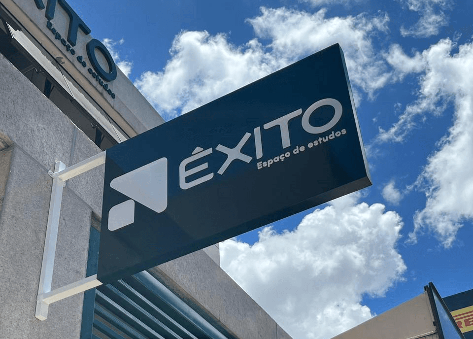 Close na placa do Êxito com logo branca no céu com nuvens